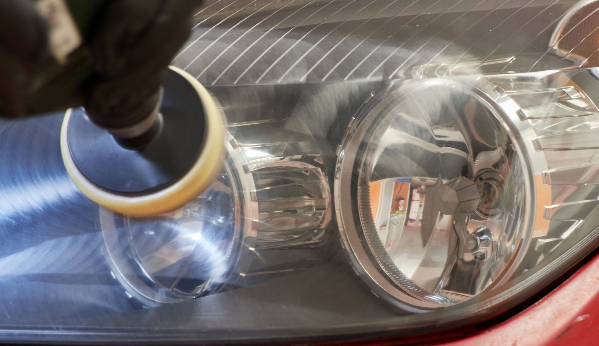 hand of a mechanic polishing the headlights of a car to make them shiny with a polishing machine